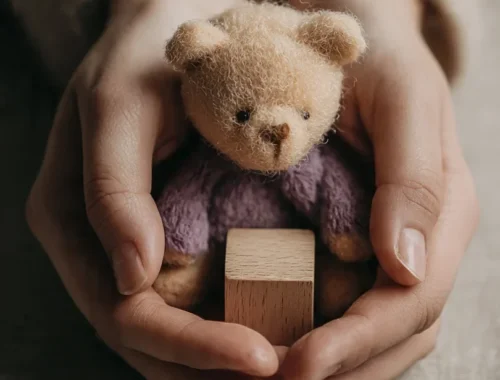 Close-up of adult hands gently holding a small child’s toy on a neutral surface, symbolising childhood trauma healing and compassionate psychological counselling.